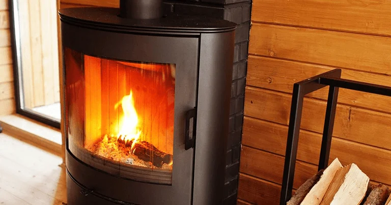 A cozy indoor scene featuring a modern black wood stove with a glowing fire, surrounded by wooden walls and a log holder.
