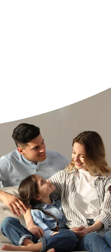 A family of four sitting together on a couch in a cozy living room, surrounded by warm lighting and decorative elements.