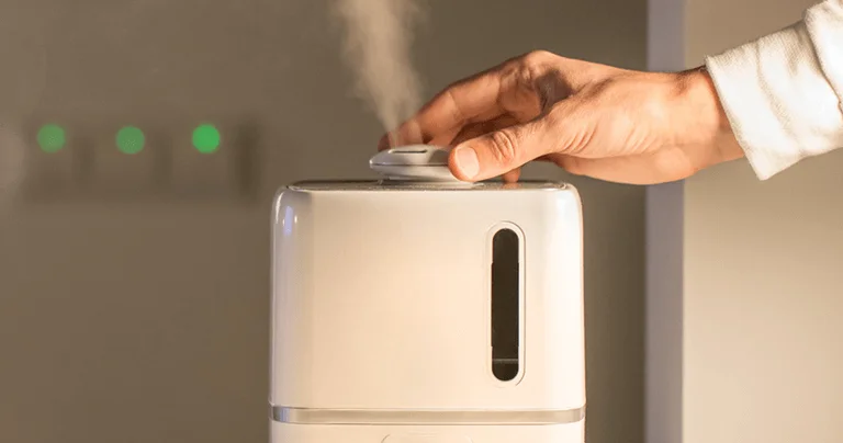 A person holds a black and white air freshener, resembling a humidifier, against a neutral background.
