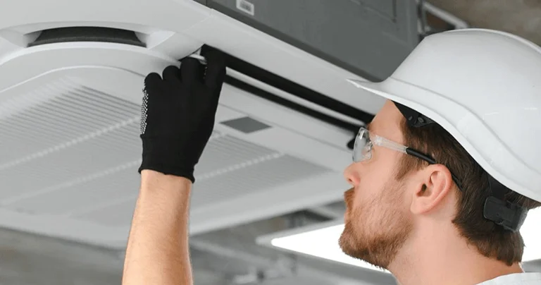A man wearing a hard hat and gloves is working on an air conditioner, demonstrating maintenance skills in a home environment.