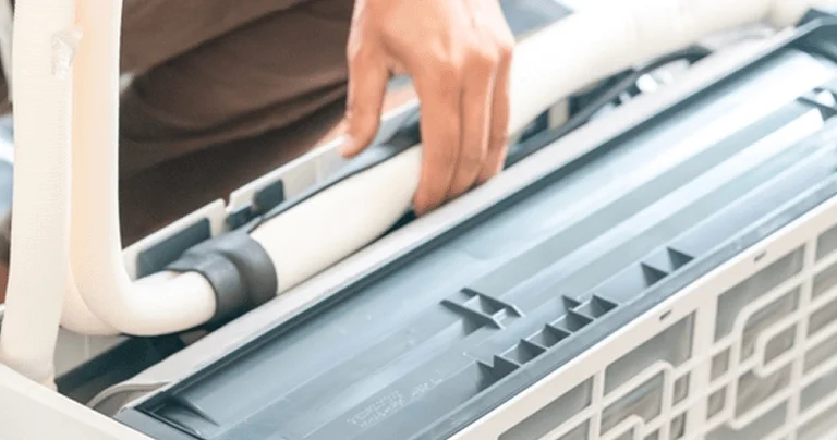 A man is repairing an air conditioner, focused on the unit with tools in hand.