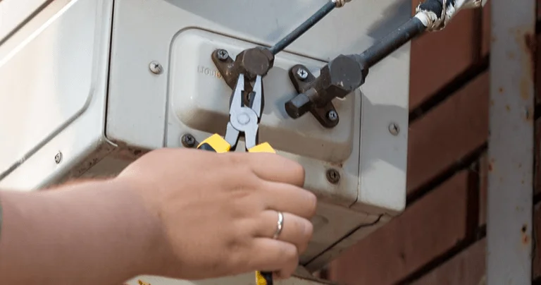 A man is repairing an air conditioner, focused on the unit with tools in hand.