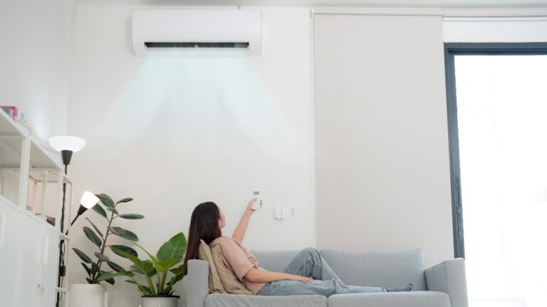 young woman lounges on a sofa, holding a remote to adjust her air conditioner