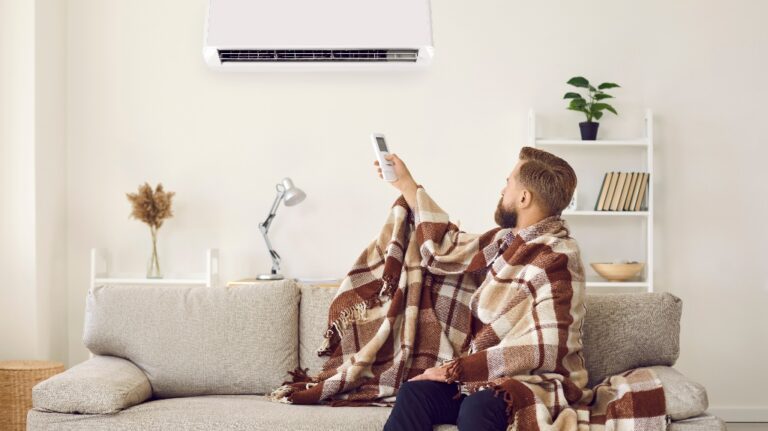 Sad angry man sitting on sofa trying to warm up