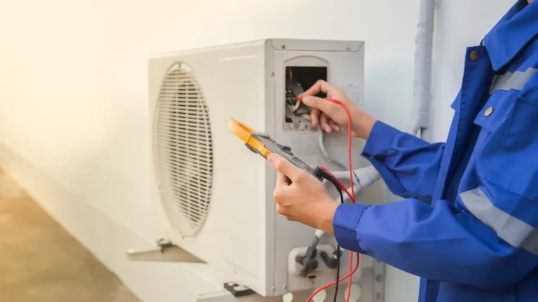 Technician in blue uniform using a multimeter to test an outdoor air conditioning unit.