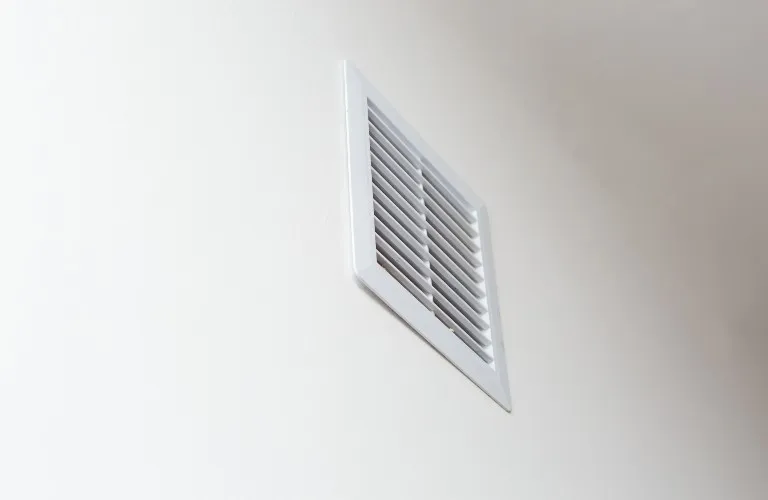 White rectangular ventilation grille installed on a smooth light beige wall.