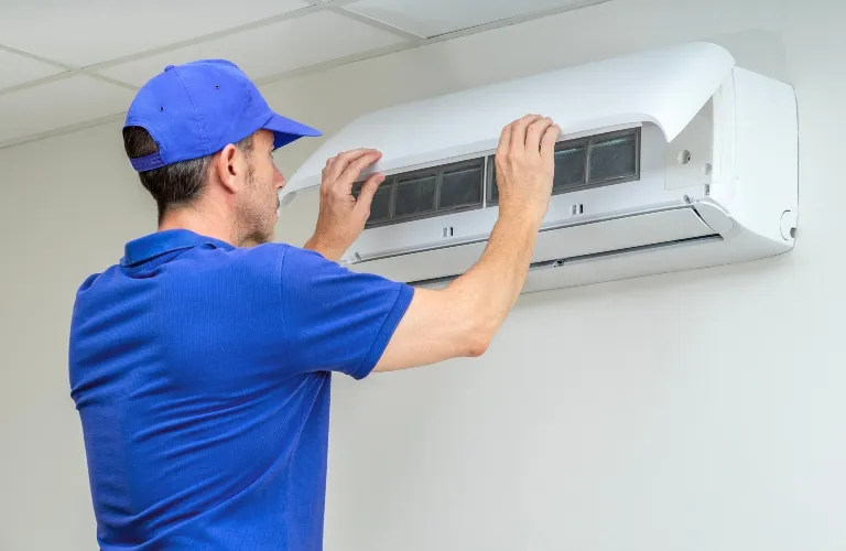 Technician in blue uniform servicing white wall-mounted air conditioning unit.