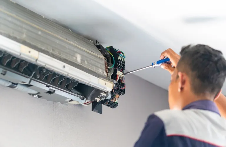 Technician using a screwdriver to repair the internal components of a wall-mounted air conditioning unit.